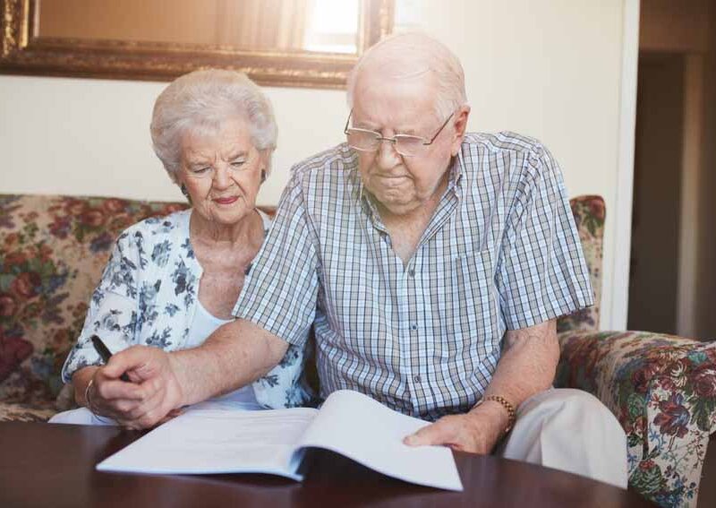 Portrait of a retired couple looking over documents while sitting at home. Senior caucasian man and woman sitting on sofa and signing some paperwork.