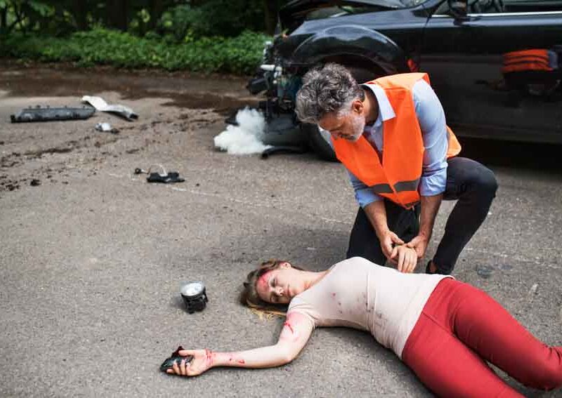 A man helping a young woman lying unconscious on the road after a car accident. Copy space.